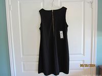 Full view of the black knee length dress hanging on a white door showing the back side with zipper.