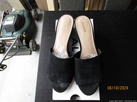 Top view of Aldo black suede mules on box showing brand and toe design.