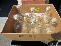Top view of 6 brandy decanters in a cardboard box showing rounded glass bodies and stoppers.
