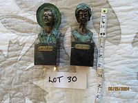Two bronze statuettes with verdigris finish, mounted on black marble blocks, with measuring tape for scale; statuette plaques read 'GARSENTI'.