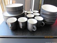 Image showing the full set of 8 plates, bowls, and coffee mugs arranged on a table, demonstrating the color scheme and heavy stoneware quality.