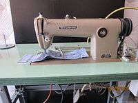 Side view of the Mitsubishi industrial sewing machine DB-150 mounted on a green table with fabric on the needle area.