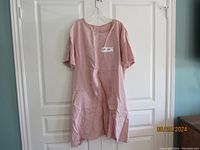 Full view of dusty pink linen dress hanging on clear hanger showing overall style and length.