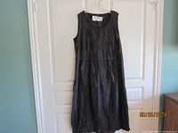 Full view of the sleeveless black Oska summer dress hanging against door, showing length and fabric texture.