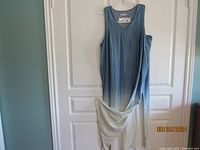 Full view of the sleeveless dress showing the cream to blue gradient and the two side splits, hung on a clear hanger against a white door.