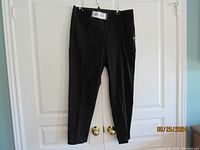Full front view of black joggers hanging on white door, showing tapered legs and elastic waistband