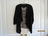 Photo showing black asymmetrical open front jacket layered over printed tank top on hanger.
