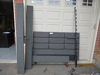 Full view of grey quilted headboard, wrapped side rails, metal slat support beam and foot rail arranged against garage door