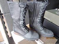 Front view of the pair of black leather boots with laces and zipper, showing rough leather texture and rubber sole.