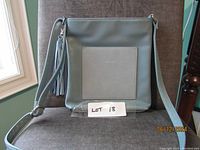 Front view of greyish blue vegan crossbody purse with a lighter grey front pocket and tassel zipper pull, sitting on a brown chair.