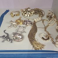 Top view of five frog brooches and jewelry laid out on a white surface with blue edge, showing details of designs and finishes.