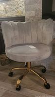 Full view of beige upholstered swivel office chair on gold metal base with caster wheels, showing scalloped backrest design and some staining.