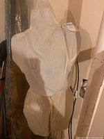 Dress form torso with white fabric cover and beige lower portion, showing wear and discoloration signs.