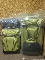 Four Ebags suitcases packaged in protective plastic, showing green soft fronts and black hard shell backs with visible telescoping handles.