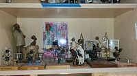 Shelf overview showing entire lot: metal dental figurines, wood/resin sculptures, framed prints and Barbie doll