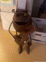 Front view of metal frog statue holding a guitar, showing wide-brimmed hat and feet details.