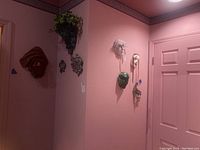 Wide view of eight decorative wall masks mounted on a pink wall, including one with faux plants decoration.