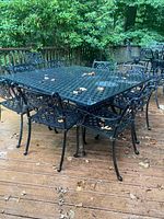 Full view of square cast metal table with eight matching chairs on a wood deck, leaves on surface