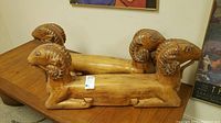 Pair of carved wood ram table base supports on wooden table, side view
