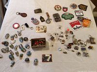 A wide view of the walking stick medallions, keychains, pins, and patches spread on a white tablecloth. Shows variety of items including box of key blanks and enamel pins.