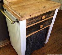 Front view showing white painted paneled side, two drawers with round knobs, fabric curtain panel below, wood floor background.