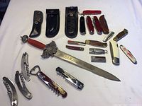 Full view of all pocket tools and cutlery including Swiss Army knives, folding knives, corkscrews, and a decorative sword with rope-wrapped handle labeled Toledo