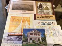 Overview photo of collection showing various posters, prints and maps related to Port Townsend, including vintage bird's eye view 1878 print, wooden boat festival and film festival posters, architectural print and maps.