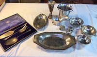 Wide view of all items included in the lot, showing serving utensils in case, napkin rings, bowls, gravy boat, pitcher, goblet, and tray.