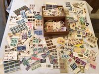 Wide view of table covered with numerous sheets and blocks of postage stamps along with loose stamps and the vintage wooden box in the center.