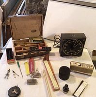 Wide view of vintage tools set including open wooden case with chisels, timer, ink bottle, drafting tools, compasses, slide rules, charcoal box, and watercolor tins.