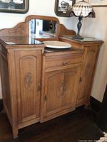 Front view of vintage carved wood buffet cabinet with side doors closed, central drawer, mirror backsplash, and marble lazy Susan on surface.