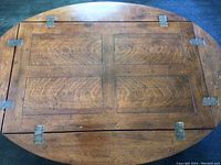 Top-down view of oval tabletop showing two hinged drop leaves, four panel design, and metal hinge hardware