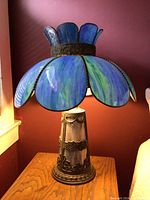 Lamp on wooden side table against maroon wall, showing flower-shaped stained glass shade in blue and green.