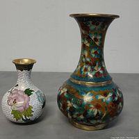 Two Chinese cloisonné enamel vases/urns shown standing side by side on a surface, highlighting size difference and detailed enamel work.