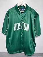 Front view of green Boston Celtics warmup shirt jacket with 'BOSTON' text and zippered front