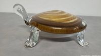 Side view of glass turtle paperweight showing brown and amber swirl shell, clear glass tail, and textured legs.