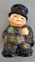 Front view of chimney sweep boy figurine showing facial details, shamrock on coat, orange scarf, and holding broom.