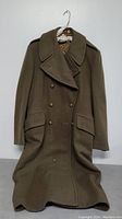 Front view of olive green men's heavy coat showing double-breasted design, lapels, front flap pockets, and buttons.