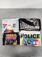 Four band t-shirts folded showing front graphic prints of Pink Floyd, Led Zeppelin, Kiss, and The Police.