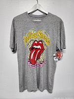 Full front view of the grey Rolling Stones T-shirt on a hanger showing the full graphic and tags.