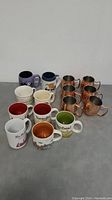 Photo showing all 15 cups including Starbucks, Tim Hortons, and six copper mugs arranged on grey surface.