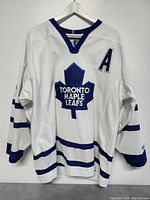 Front view of white Toronto Maple Leafs hockey jersey with team logo and captain 'A' patch.