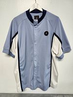 Full view of vintage Michael Jordan warmup shirt/jacket hanging on white hanger, showing front with short sleeves and blue with white panels.