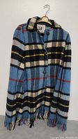 Front view of the woman's plaid wool jacket hanging on a hanger showing button closure, collar, and fringe hem