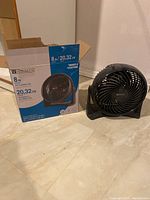 Air circulator fan next to its original box showing brand and size.