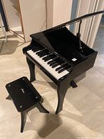 Glossy black baby toy piano with lid open and matching bench beside it, showing minor scratches.