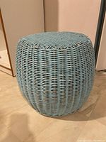 Front angle view of blue wicker stool showing round barrel shape and paint distress.