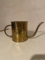 Photo showing side view of brass watering can with hammered flower pattern, handle at the back and long curved spout