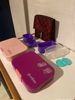 Two Yum bento boxes, various small plastic containers, small lids and a soft insulated lunch bag showing front, sides, and top overall condition.