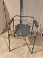 Front view of sturdy grey commode chair with padded armrests and solid seat.